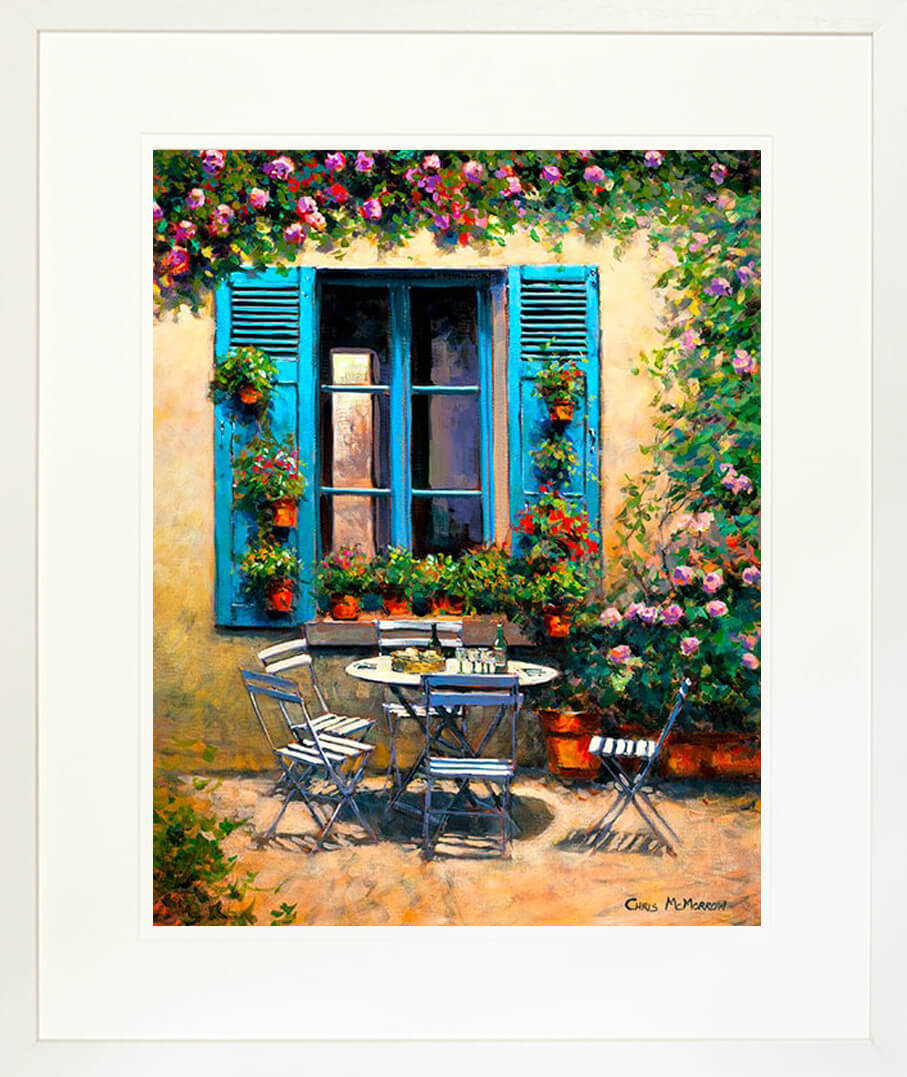 A framed print of a painting of a table and chairs set for an afternoon snack in the South of France