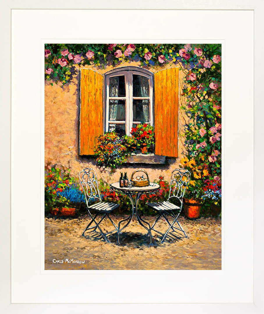 A framed print of a painting of an ornate garden table and chairs outside a yellow shuttered window on a sunny afternoon