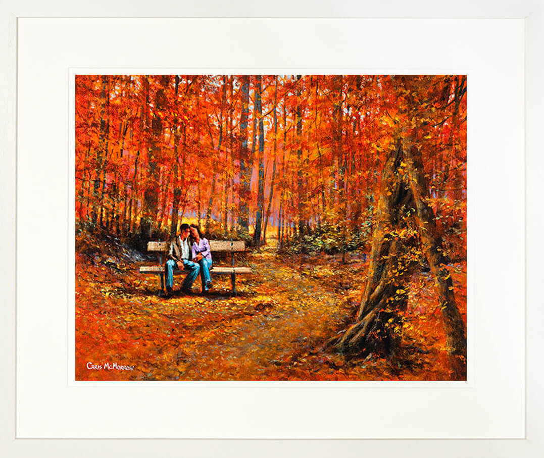 A framed print of a painting of two lovers on a bench in an autumnal forest setting