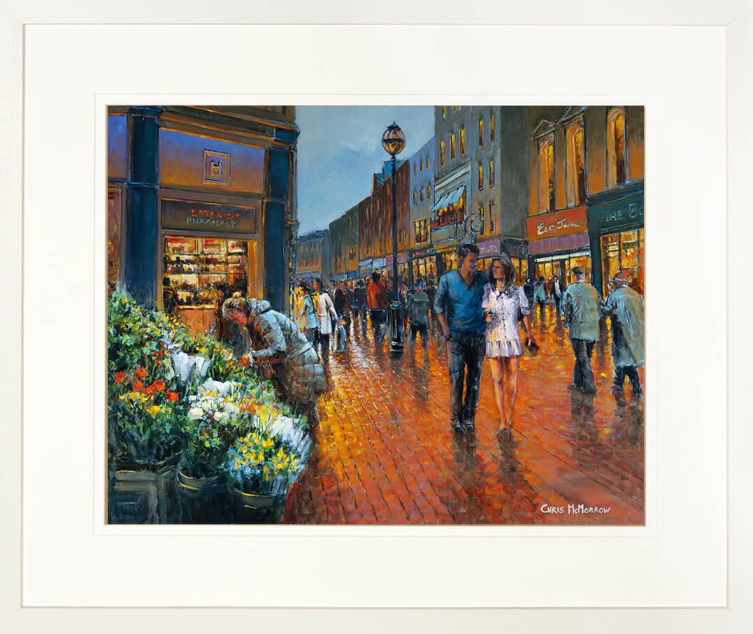 A framed print of a painting of people in Grafton Street, Dublin in the evening glow from street lamps and storefronts.